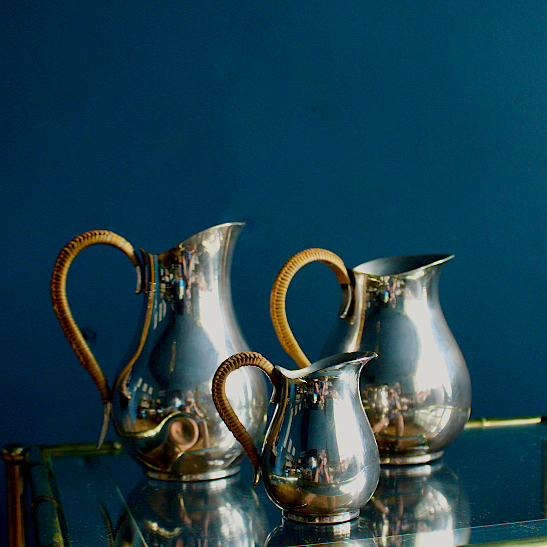 A beautiful trio set of silver plated jugs in midcentury style with wicker handles