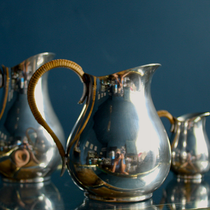 A beautiful trio set of silver plated jugs in midcentury style with wicker handles